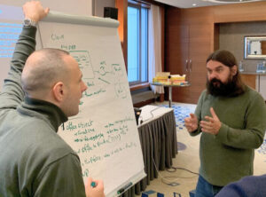 A Beard Man talking with another man in front of a flipchart